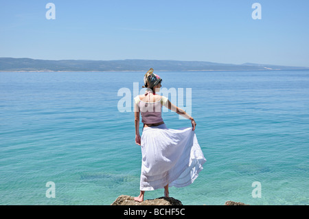Junge Frau, die auf den Felsen vom Ozean Stockfoto