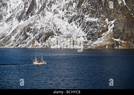 Dorsch Angeln Boot Segeln in den Gewässern des Kjerkfjorden mit Schnee bedeckt die Berge im Hintergrund in der Nähe von Reine, Lofoten Inseln, Norwegen Stockfoto