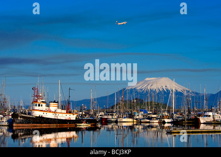 Ein Alaska Airlines Jet zieht über Mount Edgecumbe und dem kleinen Bootshafen in Sitka, Alaska Stockfoto