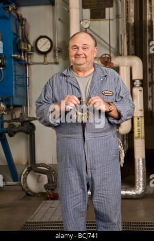 Männlichen kaukasischen im blauen Hausmeister/Hausmeister Overall in Werkseinstellung einschließlich Kessel, Rohre, Ventile.  Er hält Satz von Schlüsseln Stockfoto