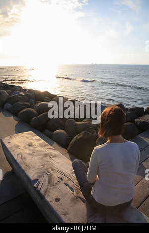 Frau sitzt auf der Bank am Meer, Neuseeland Stockfoto