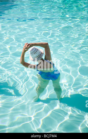 Rückseite des älteren kaukasischen weiblich mit Händen umklammert, über den Kopf tragen Hut und Badeanzug wie sie im Schwimmbad Übungen Stockfoto