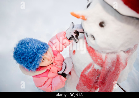 Junges Mädchen schmückt einen Schneemann mit rotem Schal und schwarzen Zylinderhut, Alaska Stockfoto