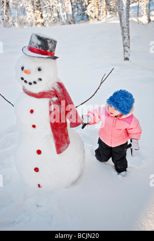 Junges Mädchen schmückt einen Schneemann mit rotem Schal und schwarzen Zylinderhut, Alaska Stockfoto