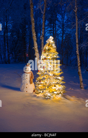 Schneemann mit rotem Schal und schwarzen Zylinderhut stand neben einem Weihnachtsbaum im Schnee bedeckt Birkenwald, Winter Stockfoto