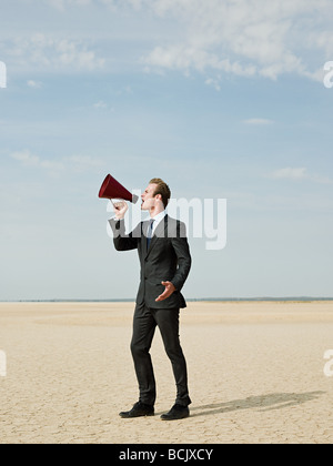 Geschäftsmann mit einem Megaphon in der Wüste Stockfoto