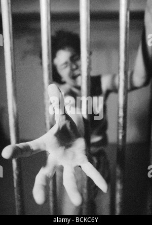 Frau hinter Gittern erreichen Hand durch Bars, b&w Stockfoto