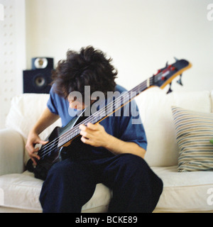 Junger Mann auf Sofa Gitarre spielen Stockfoto