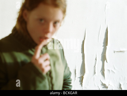 Junge Frau mit Finger auf die Unterlippe, verschwommen im Vordergrund, abblätternde Farbe an der Wand im Hintergrund Stockfoto