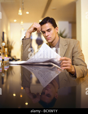 Mann im Anzug sitzt am Tisch, liest Zeitung Stockfoto