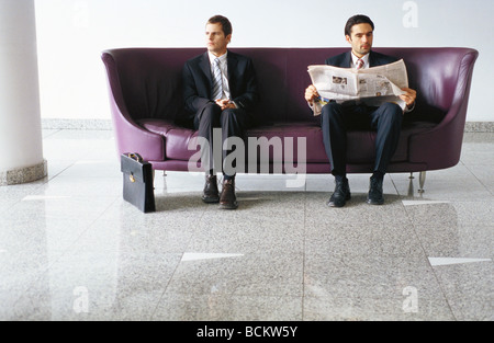 Zwei Geschäftsleute auf Sofa, einer Lesung Zeitung Stockfoto