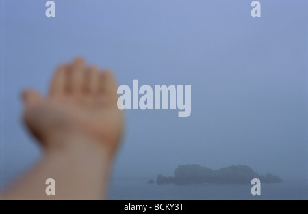 Person die Hand, verschwommen, vor Felsen im Meer Stockfoto