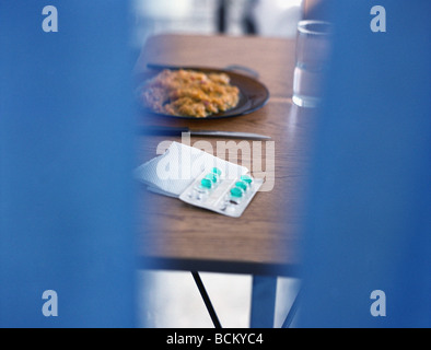 Teller mit Essen und Packung Pillen auf Tisch, gesehen durch die Öffnung im Vordergrund Stockfoto