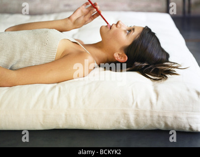 Junge Frau liegen auf der Matratze, mit Bleistift in Mund, Seitenansicht Stockfoto