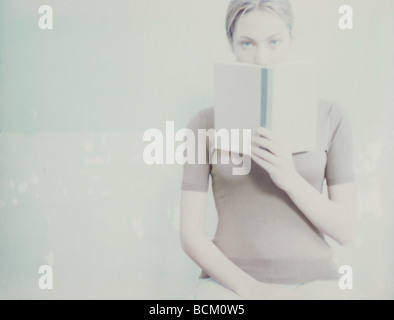 Frau, Blick in die Kamera über offenes Buch Stockfoto