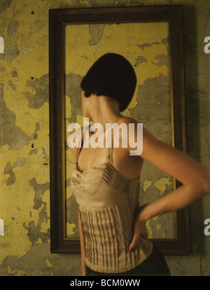 Frau stehend mit Hand auf Hüfte, auf der Suche über die Schulter bei leeren Rahmen an der Wand hängen Stockfoto