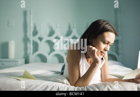 Frau auf Bett liegend mit Hand unter Kinn, Brief lesen Stockfoto