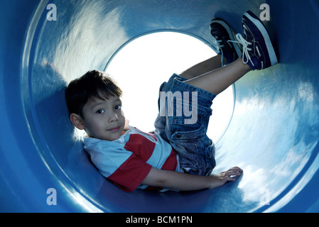 Junge sitzt im Spielplatz-Tunnel mit Beine hoch, Blick in die Kamera, in voller Länge Stockfoto