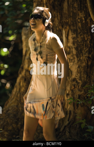 Junge Frau mit Sonnenbrille im Freien stehen, zuhören, Kopfhörer, Lächeln Stockfoto
