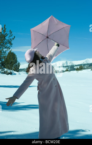 Teenager-Mädchen stehen im Schnee, Regenschirm, Arme hochhalten Stockfoto