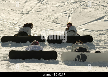 Vier junge Snowboarder auf Skipiste sitzen, hinten sehen, ein Blick über die Schulter Stockfoto