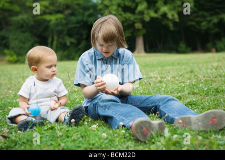 Mädchen mit Down-Syndrom sitzen mit kleinen Bruder auf dem Boden, beide spielen mit Bällen Stockfoto