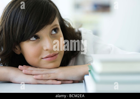 Junge, weibliche Kopf auf Händen ruhen, blickte verträumt, Stapel von Büchern im Vordergrund Stockfoto