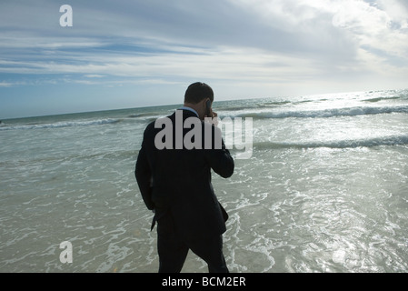 Geschäftsmann in Brandung am Strand, Wandern, reden über Handy, Rückansicht Stockfoto