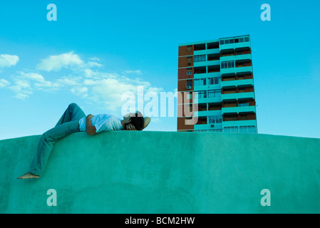 Junger Mann am Ledge, Blick auf Himmel, Wohnung Hochhaus im Hintergrund liegen Stockfoto