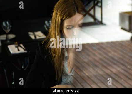 Junge Frau sitzt allein im Café, angesehen durch Fenster Stockfoto