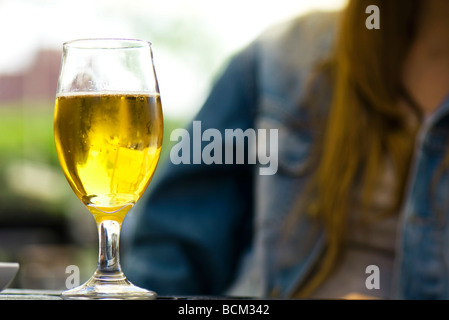 Glas Bier auf Tisch, junge Frau im Hintergrund Stockfoto