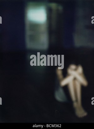 Frau sitzt am Boden mit Kopf auf Knie, unscharf gestellt Stockfoto