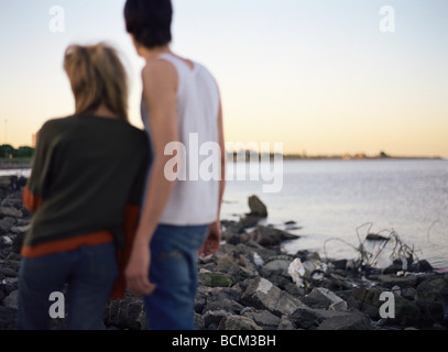 Junges Paar auf felsigen Strand übersät mit Müll, Blick auf Sonnenuntergang, Rückansicht Stockfoto