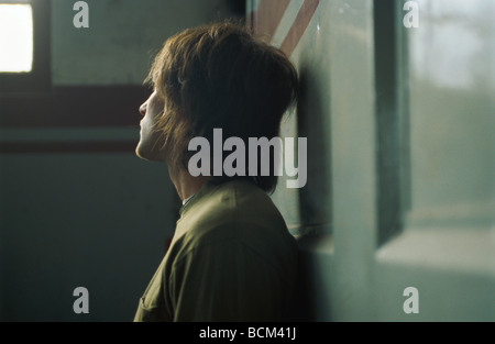 Junger Mann Wand gelehnt, blickte zu Fenster Stockfoto