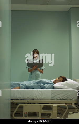 Frau liegend auf Krankenhausbett, Blick in die Kamera, Krankenschwester, Blick auf Tabelle im Hintergrund Stockfoto