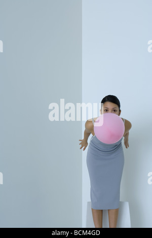 Frau bücken, Ballon im Mund halten, Blick in die Kamera Stockfoto