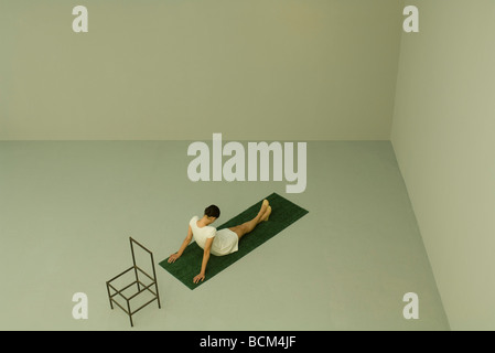 Frau sitzt auf Kunstrasen mit Kopf nach unten, leeren Stuhl hinter ihr, erhöhte Ansicht Stockfoto