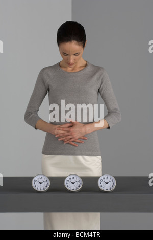 Frau stehend mit den Händen auf Magen, blickte, Uhren aufgereiht vor ihr Stockfoto