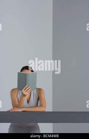 Frau sitzt am Tisch lesen, Gesicht verdeckt durch Buch Stockfoto