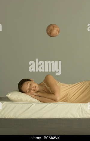 Frau schläft im Bett, Kugel in der Luft über ihr schweben Stockfoto