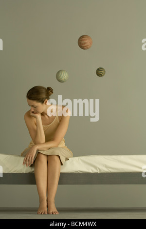 Frau sitzt auf dem Bett, hand unter Kinn, Sphären schweben in der Nähe von Kopf Stockfoto