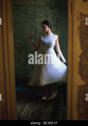 Frau in weißem Kleid, tanzt mit geschlossenen Augen, betrachtet durch Tür Stockfoto