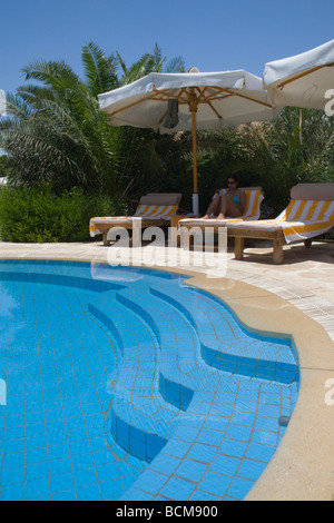 Eine junge Frau entspannt auf einer Sonnenliege am Pool im Schatten eines Sonnenschirms Stockfoto