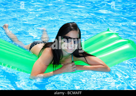Attraktive schlanke und gebräunte junge Dame liegen auf aufblasbare Liege am sonnigen Swimmingpool auf Urlaub oder Ferien Stockfoto