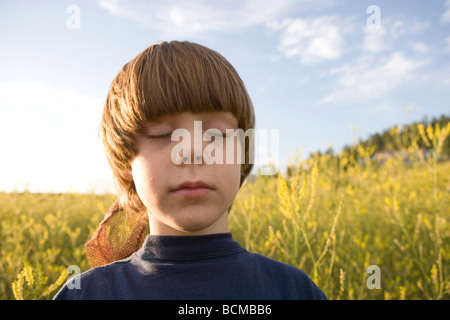 sieben Jahre alter Junge singen seine Augen schließen und hören die Vögel in einem Feld von Wildblumen, Pagosa Springs, Colorado Stockfoto