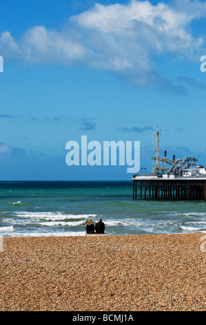 Zwei Personen sitzen auf der Kiesstrand in der Nähe von Brighton Pier in Sussex. Foto von Gordon Scammell Stockfoto