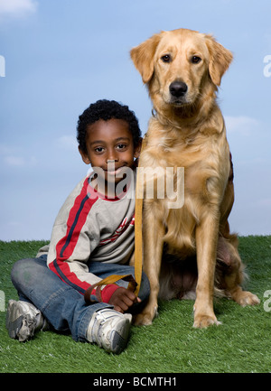 African American Boy und ein Golden Retriever, sitzen auf dem Rasen, 1 Jahr alt, vor blauem Himmel, Studio gedreht Stockfoto