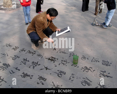 Chinesischer Mann üben Kalligraphie auf den Zement gemahlen mit chinesischen Pinsel und Wasser, Shanghai, China Stockfoto