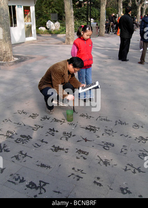 Chinesischer Mann praktizierender Kalligraphie auf den Zement mit chinesischen Pinsel und Wasser, während ein junges Mädchen auf Erden, Shanghai, Stockfoto