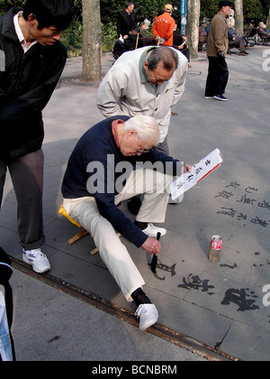 Ältere Chinesen üben Kalligraphie auf dem Boden mit chinesischen Pinsel und Wasser, während andere suchen auf Zement, Stockfoto